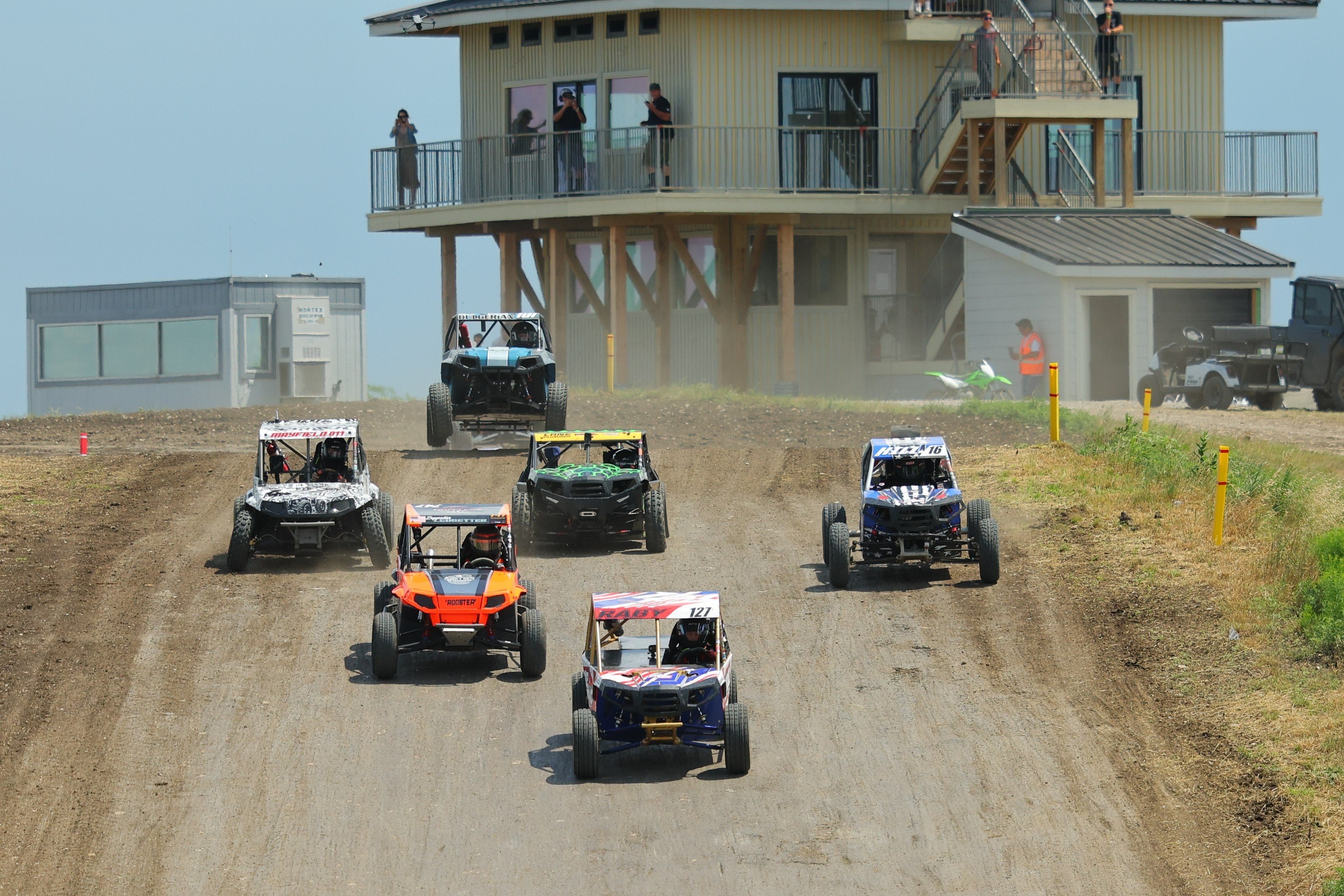Side-by-side race field descending a dirt straightaway