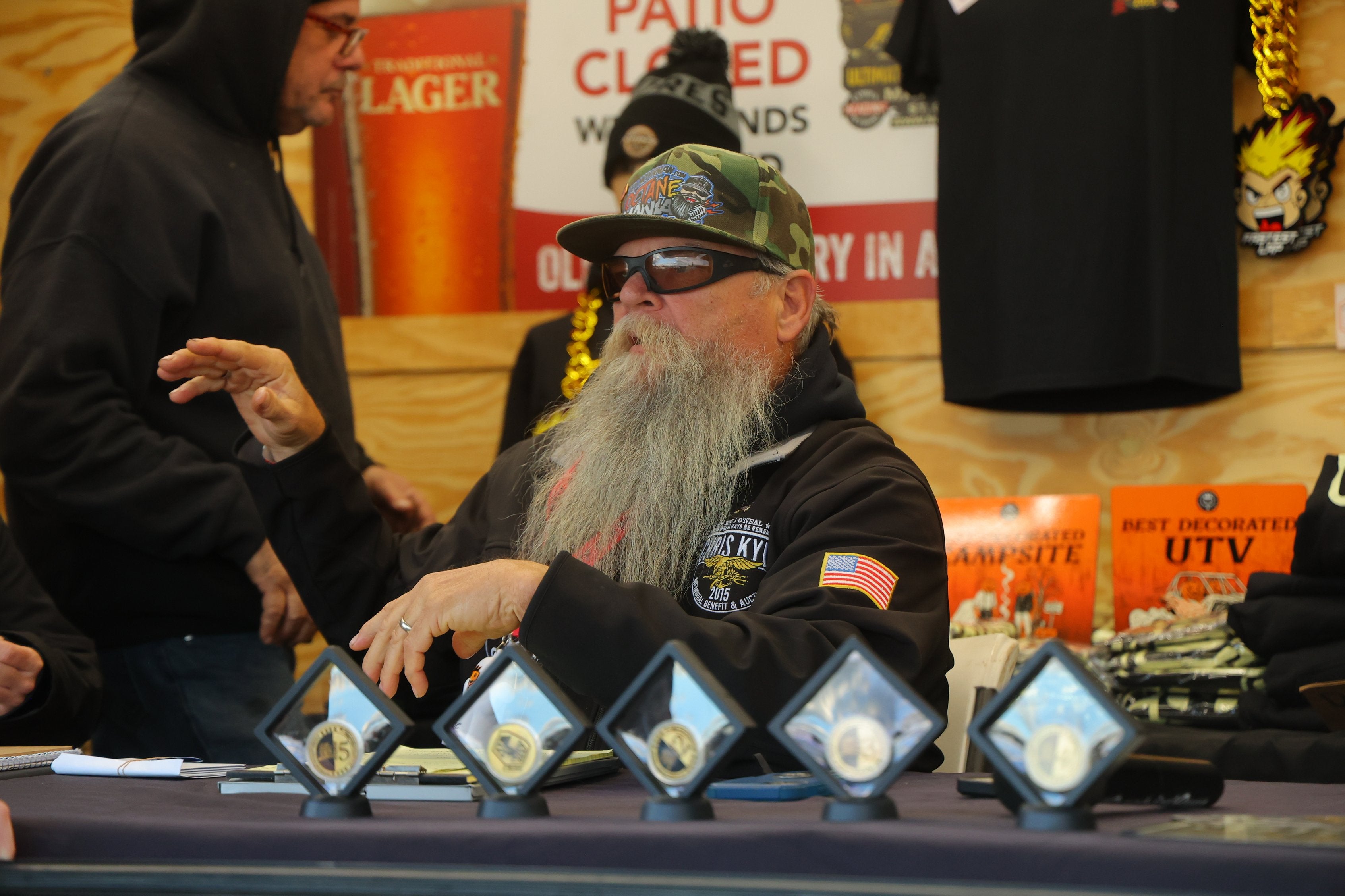 Bearded race official seated behind event trophies